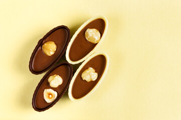 Four chocolates with nuts on a yellow background. View from above.