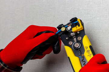 An electrician in red gloves is using wire cutters to remove insulation from electrical wires.