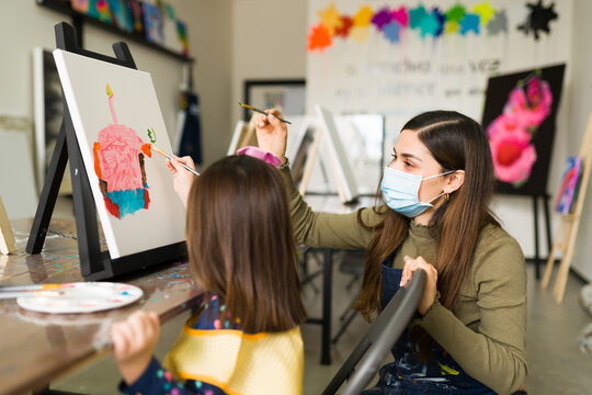 Side view of a young teacher teaching a little girl to paint