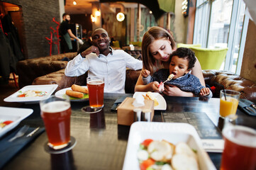 Happy multiethnic family with boy kid spend time at restaurant. Relationships of african man and white european woman.