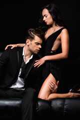 Fototapeta na wymiar man with closed eyes touching leg of seductive woman in dress isolated on black