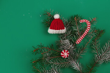 decorative knitted ornamentshat and caramels in red and white color on fir-tree snow branch and green background