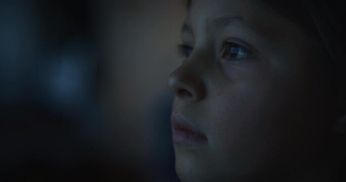 Cinematic macro shot of curious happy little girl while watching television screen in the dark. Concept of technology, new generation, family, connection, vision of the future of children with web.
