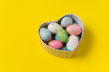 Heart shaped box with colorful Easter eggs on bright yellow background. Holiday eggs.