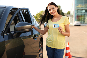 Happy young woman holding license near car outdoors. Driving school