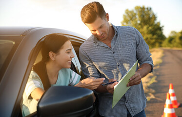 Instructor with clipboard near his student in car outdoors. Driving school exam