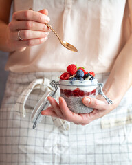 A woman holding a golden spoon and a mason jar with vegetarian chai pudding  topped with fresh berry fruit 
