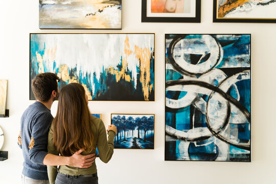 Rear view of a young woman and guy admiring the paintings of an art exhibition