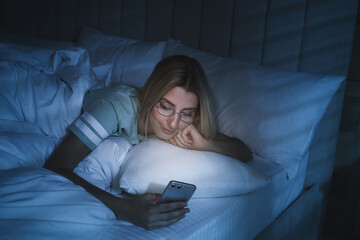 Young woman using smartphone in bed at night. Nomophobia and sleeping disorder problem