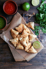 Samosa - fried/baked pastry with filling, popular Indian snacks, served in bowl with spices and fresh cilantro on rustic background
