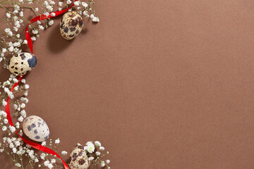 Minimalism style Easter background with beautiful white spring flowers, quail eggs and red ribbon on natural brown background. Zero waste eco friendly Easter decorations concept.