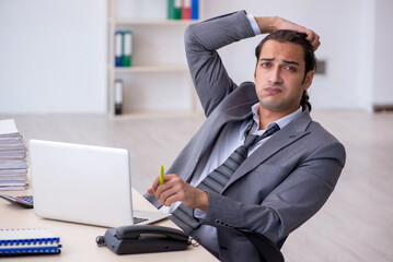 Fototapeta premium Young male employee unhappy with excessive work in the office