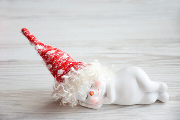 cute white sleeping snowman in a red hat on light wooden background. Christmas and New Year concept. sleeping snowman