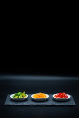 Three small tasting plates with red, yellow and green peppers on a black plate and copy space above