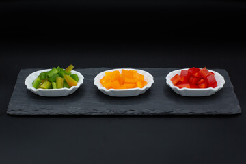 Small tasting plates with red, yellow and green peppers on plate and black background