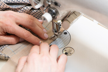 Obraz na płótnie Canvas Woman hand guiding white cloth through a sewing machine. Close-up view.