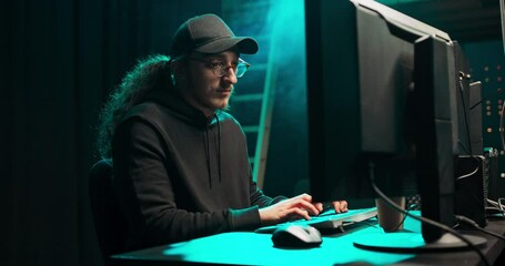 Middle aged Hackers with curly long hair in a sweatshirt, baseball cap and glasses making cryptocurrency fraud using virus software and computer interface. Blockchain cyberattack, ddos and malware - Powered by Adobe