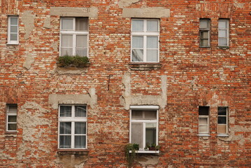 Aged red brick wall texture of house facade with windows. Old grunge wall surface background pattern of masonry