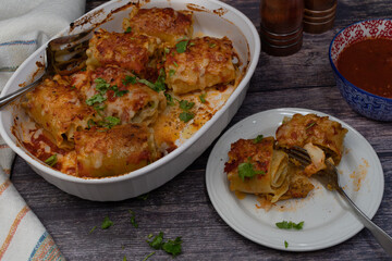 Vegetarian lasagna rolls filled with seitan in white dish on wooden table