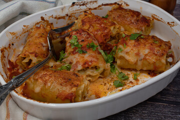 Vegetarian lasagna rolls filled with seitan in white dish on wooden .table, close up