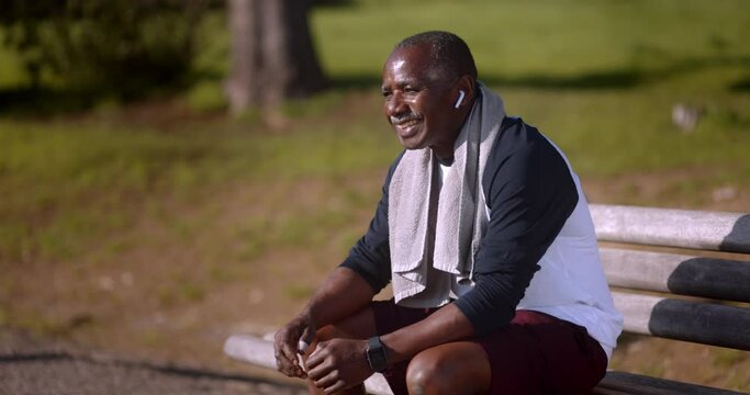 Senior african-american man with earphones sitting on bench after exercise