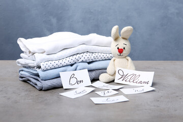 Paper sheets with different baby names, toy and child's clothes on grey table