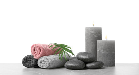 Spa stones, towels, candles and tropical leaf on light grey table against white background