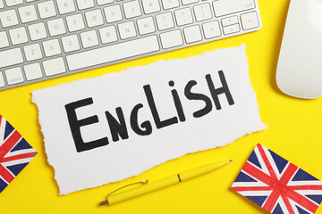 Paper with word English, keyboard, mouse and UK flags on yellow background, flat lay