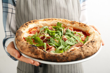 Woman holding tasty pizza with meat and arugula on white background, closeup