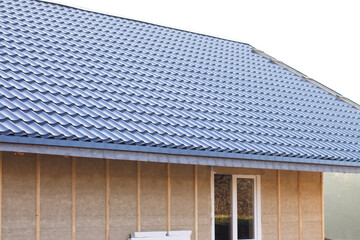 Gray metal roof of a house under construction with vertical beams and a waterproof membrane for wall cladding