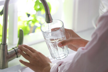 Woman pouring water into glass in kitchen, closeup