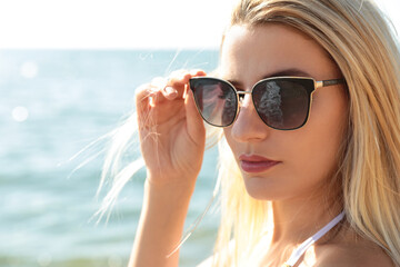 Beautiful woman wearing sunglasses near sea on sunny day, closeup