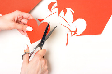 The girl cuts out a heart shape from red cardboard with scissors for decoration. Preparation for Valentine's Day. Top view layout