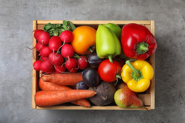 Wooden crate full of different vegetables and fruits on grey table, top view. Harvesting time