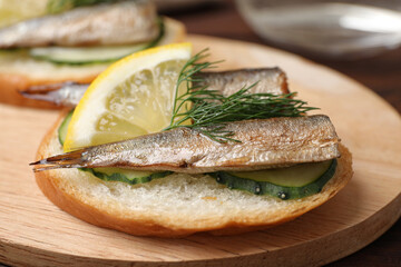 Delicious sandwich with sprats, cucumbers, lemon and dill on wooden board, closeup