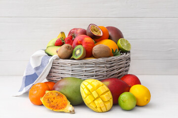 Assortment of fresh exotic fruits in basket on white wooden table