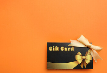 Gift card with bow on orange background, top view. Space for text