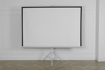 Blank projection screen near white wall indoors. Space for design