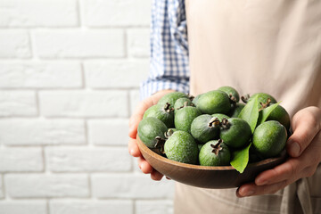 Woman holding fresh green feijoa fruits against white brick wall, closeup. Space for text