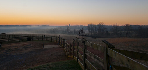 A view of a fence and weather vane during sunrise in Virginia.
