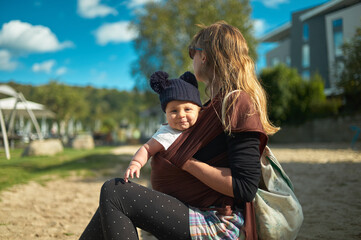 Young mother with baby in sling in the park on sunny autumn day