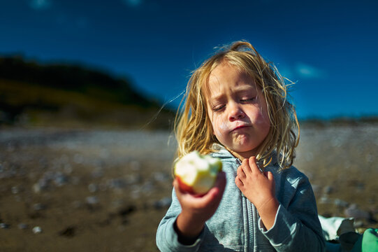Preschooler eating an apple on the beach in autumn