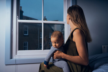 Young mother sitting by the window with her baby