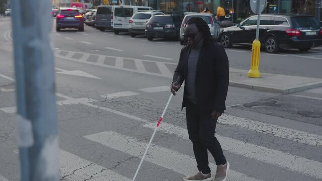 Blind african american black man crossing over the crosswalk with his walking stick. High quality 4k footage