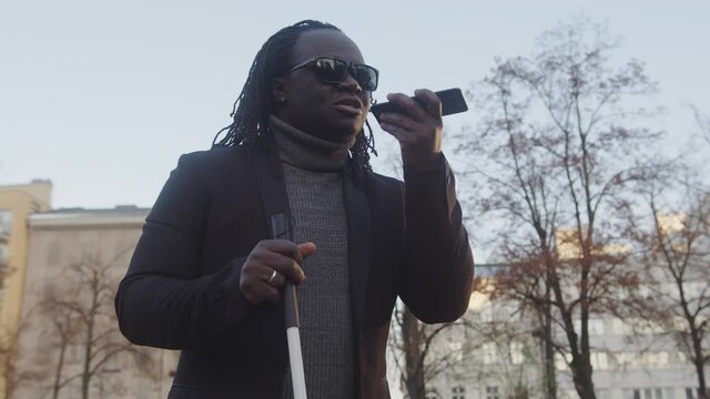 Blind black african american man having a phone conversation outside while holding his walking stick. High quality 4k footage