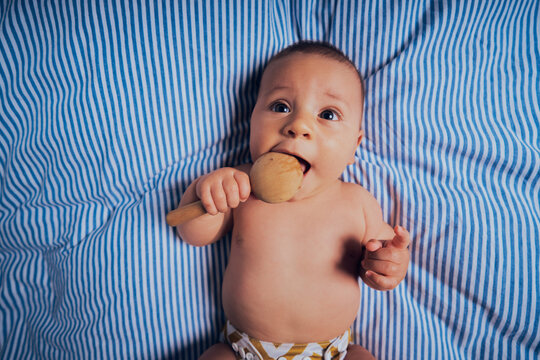 Baby on bed with wooden rattle