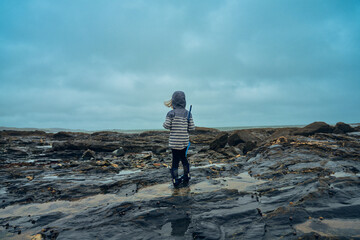 Preschooler standing on rocks by the sea with a fishing net