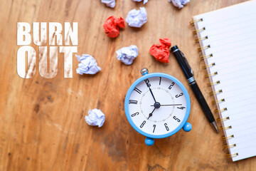 top view of an alarm clock, a pen, a notebook, crumpled papers, and a message on burnout written on...