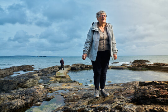Senior woman standing on rocks by the sea in autumn