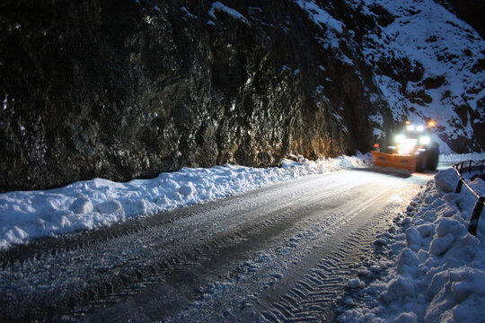snowplow passes through the snowy mountain streets in the evening to clean up the road traffic